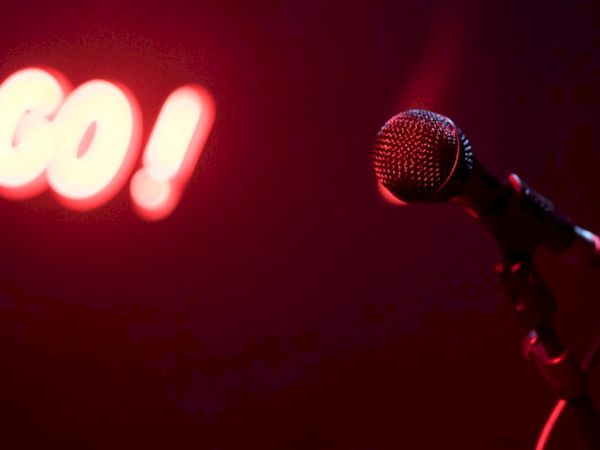 A microphone is illuminated on stage under a red spotlight, with the word "GO!" glowing in the background.