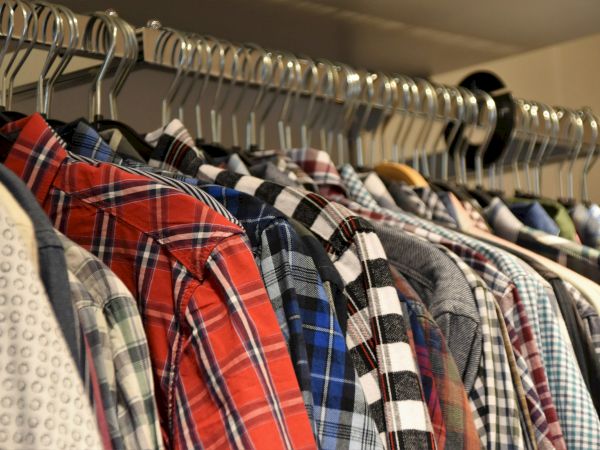 A row of various patterned shirts, including plaids and checks, hangs neatly on metal hangers in a closet.