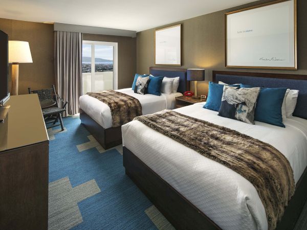 A modern hotel room with two double beds, stylish decor, a TV, and a window view, creating a cozy and inviting atmosphere.