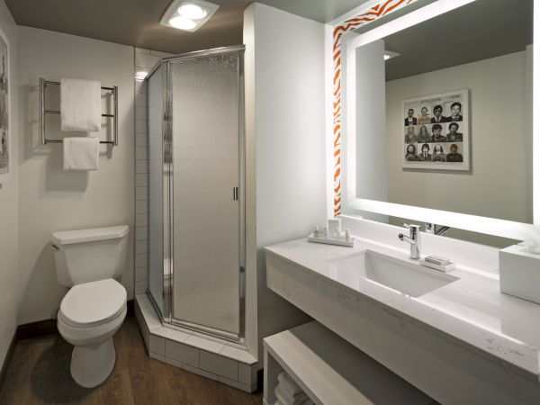 A modern bathroom with a toilet, a glass shower, a sink with a lighted mirror, towel rack, and wall art.