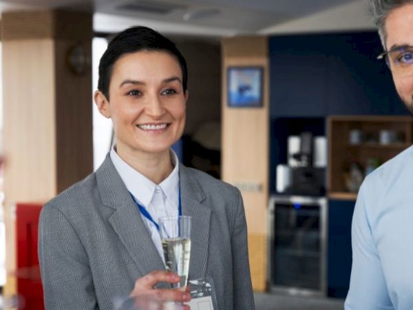 A group of people at a social gathering, wearing name badges, smiling, and holding drinks.