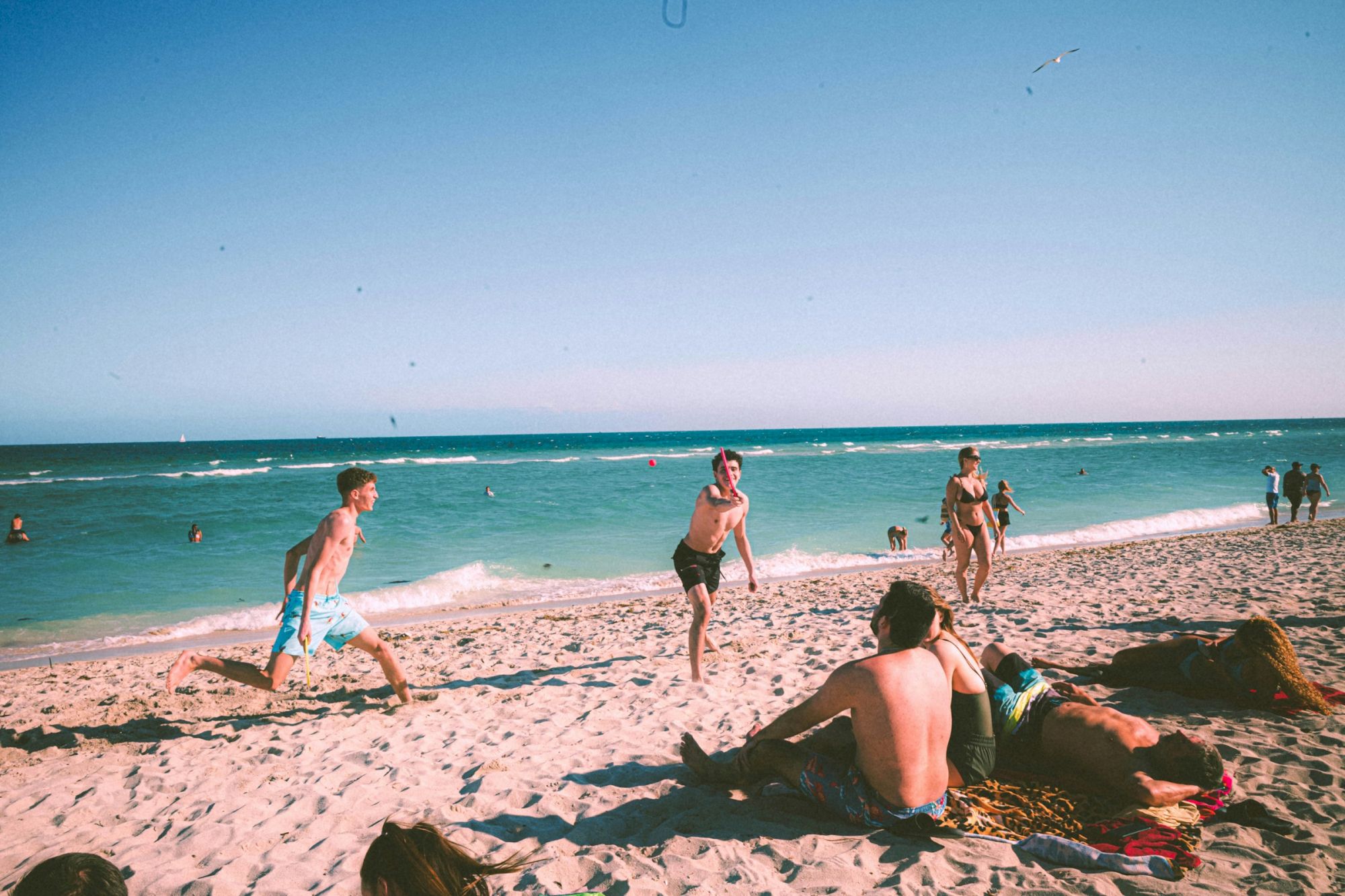 People enjoying a sunny day at the beach; some are playing, others are relaxing by the ocean.