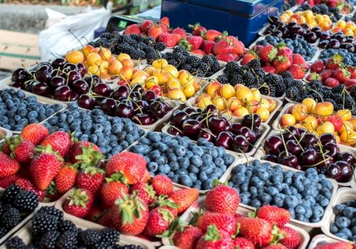 A colorful display of assorted berries and cherries in containers at a market stall, including strawberries and blueberries.