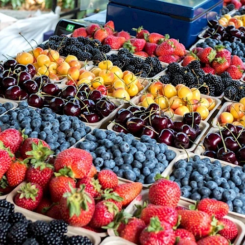 A colorful display of assorted berries and cherries in containers at a market stall, including strawberries and blueberries.