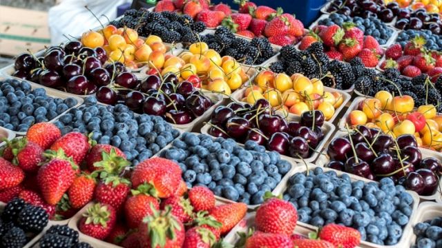 A colorful display of assorted berries and cherries in containers at a market stall, including strawberries and blueberries.