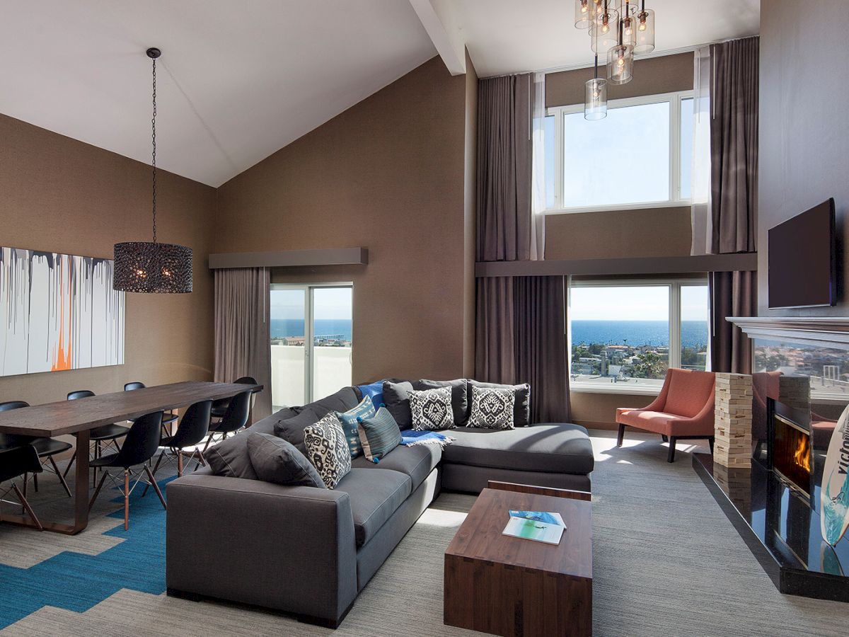 A modern living room with a sectional sofa, dining table, fireplace, wall art, and ocean view windows.