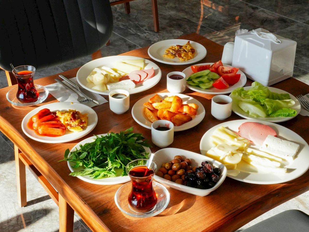 A table with a variety of breakfast foods including cheeses, vegetables, olives, and tea is set up for a meal.