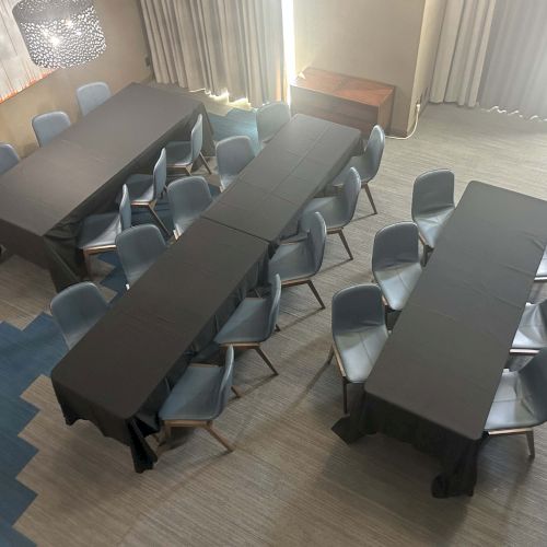 The image shows a conference room setup with black tablecloths and gray chairs, arranged in a U-shape.