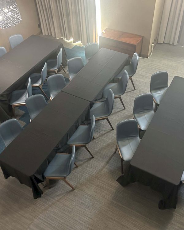 The image shows a conference room setup with black tablecloths and gray chairs, arranged in a U-shape.