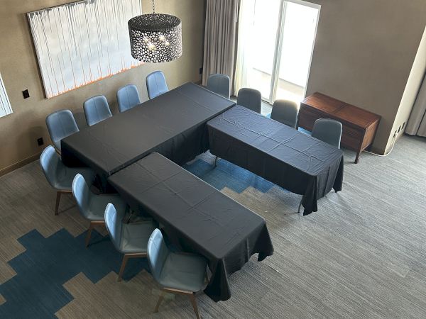 A conference room with U-shaped tables, chairs, a pendant light, window, and wall art on an accented floor.