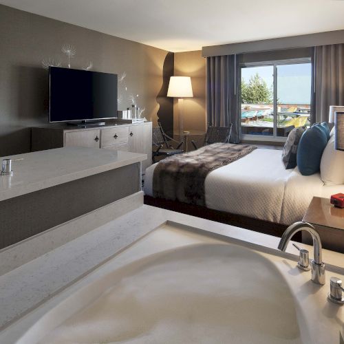 A modern hotel room features a bed, a TV, a bathroom area, and a window with a view, creating a cozy and stylish atmosphere.