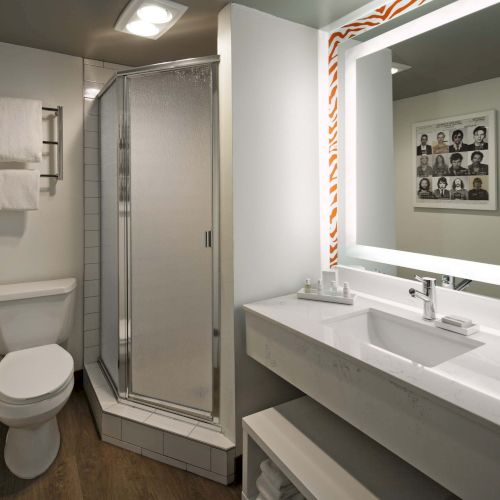 A modern bathroom with a shower, toilet, and a sink. There's a large mirror and a towel rack with towels.