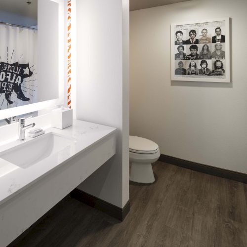 A modern bathroom features a sink, a toilet, decorative curtains, and a wall photo collage.