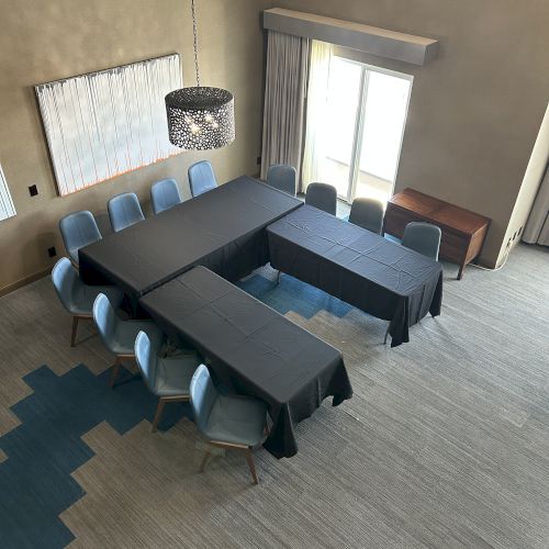 A U-shaped conference table setup with black tablecloths and chairs in a room with carpet and wall decor.