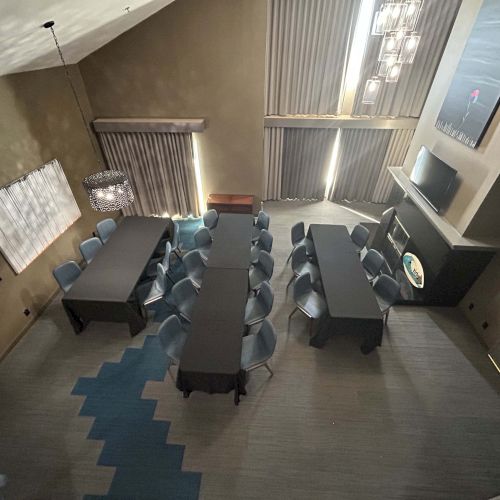 The image shows a conference room with tables arranged in a U-shape, surrounded by chairs, modern lighting, and abstract wall art.