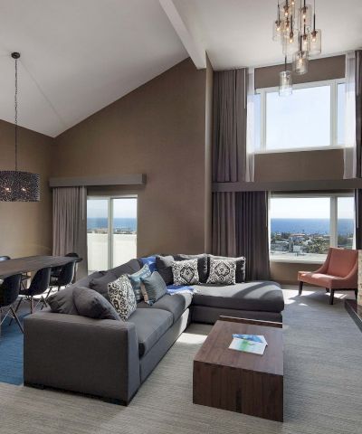A modern, open-concept living area with a gray sectional, floor-to-ceiling windows, a fireplace, and a dining space&mdash;cozy and stylish, with a view.