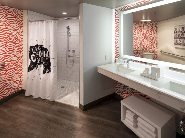 A modern hotel bathroom with red zebra-patterned walls, a shower with a bold curtain, and a white vanity and mirror.